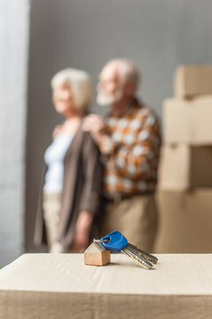 blurred view of senior couple moving into new house and keys on foreground, moving concept