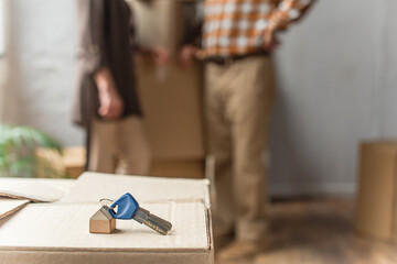 Fototapeta na wymiar keys lying on cardboard box on foreground and blurred view of senior couple, moving concept