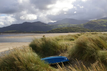 A blue rowing boat stored between the marram grass on the Mawddach Estuary, Gwynedd, Wales, UK