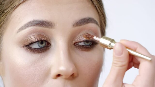 Extreme close up shot of young woman applying shimmering metallic eyeshadow to her eyelid while doing makeup