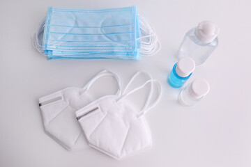 Obraz na płótnie Canvas Hand sanitizers and respiratory masks on white background, flat lay. Protective essentials during COVID-19 pandemic