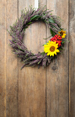 Beautiful autumnal wreath with heather flowers hanging on wooden background. Space for text