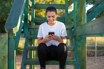 Young beautiful woman wearing sport clothes in the forest very happy and smiling, sitting and chatting on the phone