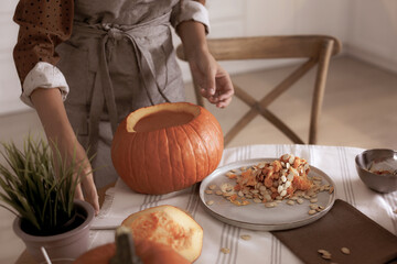 Woman making pumpkin jack o'lantern at table indoors. Halloween celebration
