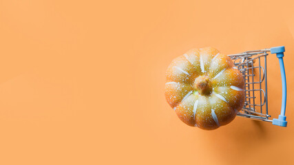 Grocery cart with pumpkin on orange background. Halloween or Thanksgiving day preparation. Flat lay, top view. Banner.