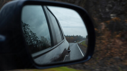 the car drives along the road at dusk and the road, nature and other car are reflected in the rearview mirror