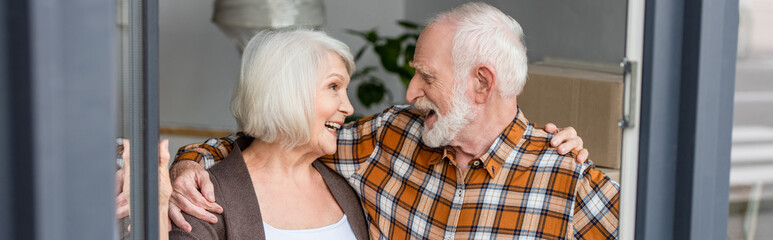 panoramic shot of laughing senior couple looking at each other and moving to new house
