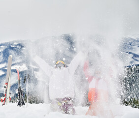 Two skiers throwing fresh powder snow high in the air. Man and woman having fun at ski resort with beautiful mountains on background. Concept of winter sport activities, fun and relationships.