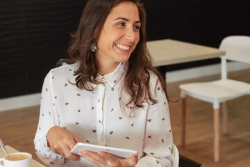 Close-up of young cheerful woman using a tablet pc while having coffee. Woman smiling having a look at the content of her social networks