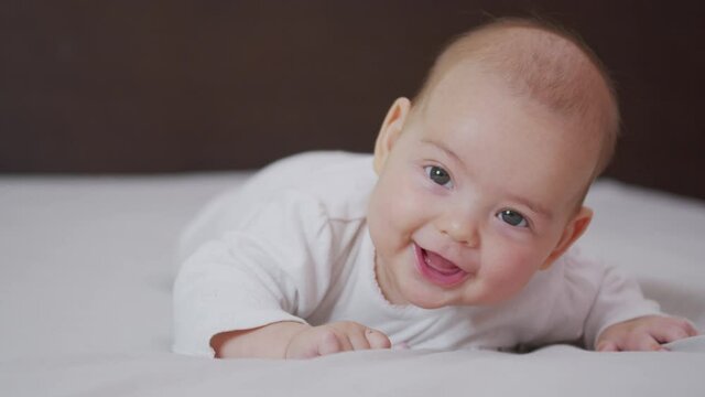 Beautiful Smiling Baby: A gorgeous little baby lies on the bed and smiles at the camera with a nice soft focus background.
