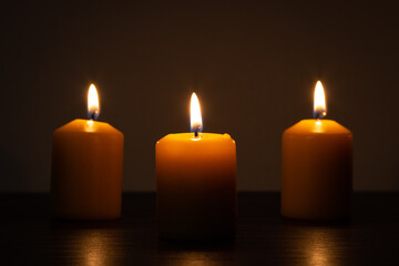 Fototapeta na wymiar Three lit candles burning in the darkness. Golden tones with selective focus and background blur