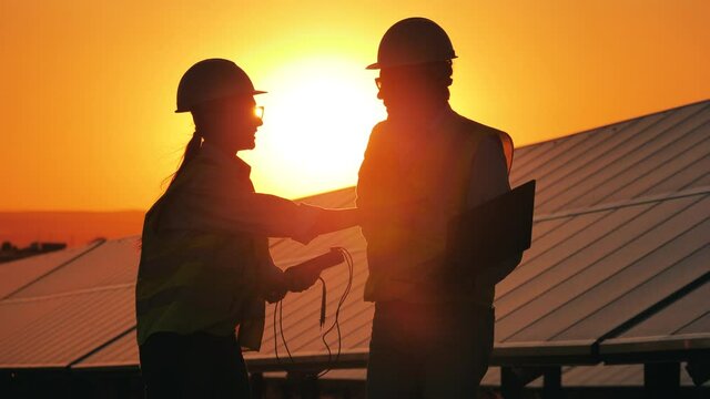 Two power workers are talking next to sunlit solar batteries