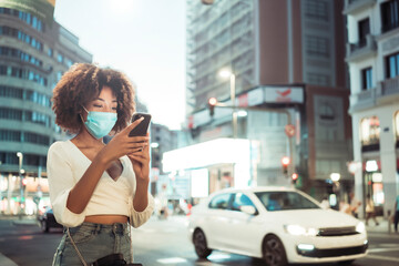 Afro woman with surgical mask using mobile against city at night