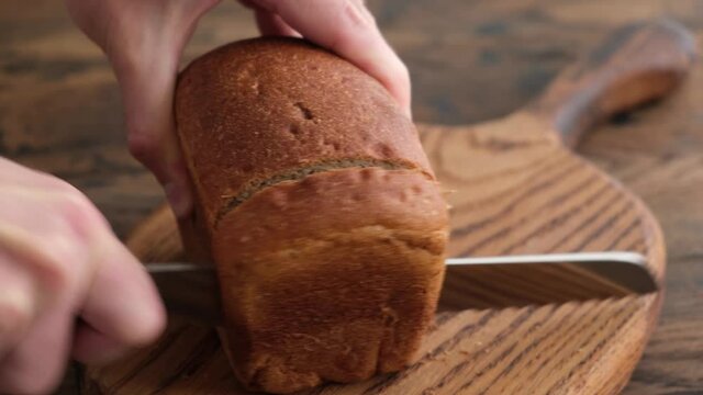 Cutting loaf of sourdough bread with sharp bread knife on a wooden table background