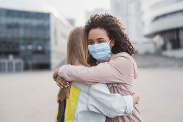 Meeting of two happy friends hugging in the street wearing protective face mask - Multiethnic young...