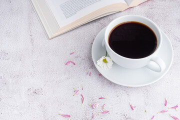 Cup of white coffee with a book and flowers on gray stone background. Space for text. Selective focus. Relax time. Concept of relax time