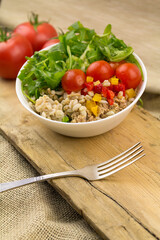 Salad with tuna, bunches and vegetables, fork and wooden table