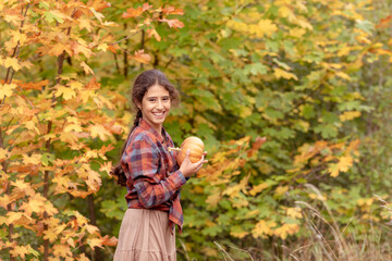 Portrait of beautiful cheerful girl with a pumpkin on a background of autumn trees celebrating...