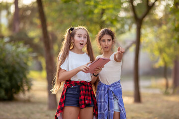 Two beautiful girls watch media content online a tablet outdoors in a park.