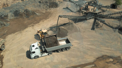 Excavator is pouring the coal into the truck. Big heaps of stones on the background.