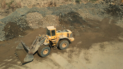 Digger machine and heaps of stones. Sand with mud and tracks of wheels.