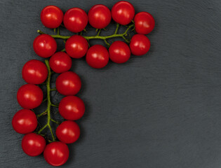 A branch of red cherry tomatoes on a dark slate background. Small and juicy vegetable is rich in vitamins and trace elements. Healthy food. Fresh and organic vegetables. Raw food