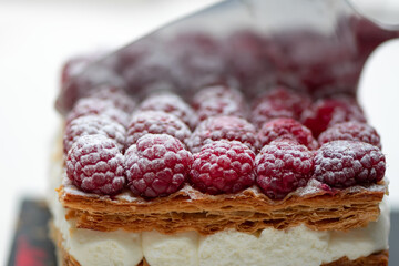 Spatula cutting a fresh raspberries cake with powdered sugar.