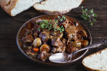 Bowl of Beef Bourguignon garnished with fresh lemon thyme and served with homemade artisan bread over a rustic wood background.