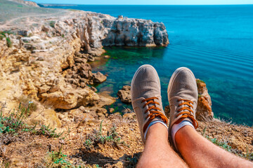 Men's feet with sneakers on the background of a stunning landscape with turquoise sea and rocks, Crimea