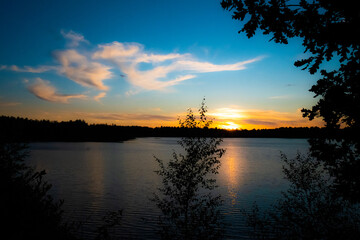 Panorama of a gorgeous sunset at a forest lake, with gold and blue color in the sky and trees reflected in the water. High quality photo