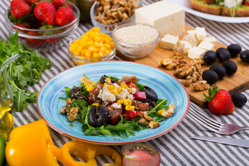 Salad with arugula, olives, Feta cheese, corn and walnut and its ingredients in the kitchen.