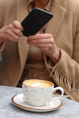 A woman using mobile phone to take a photo of coffee in Cafe