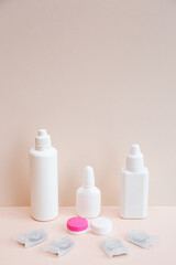 Contact lenses, lens solution and lens containers on a light pink background. Health care concept