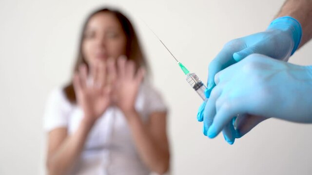 Scared woman does not want an injection. Fear of the vaccine for COVID-19. Close-up of syringe.
