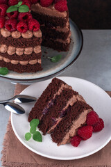 A piece of chocolate cake with raspberries and butter cream on  white table and dark backdrop. Vertical orientation.