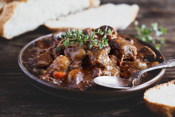 Bowl of Beef Bourguignon garnished with fresh lemon thyme and served with homemade artisan bread over a rustic wood background table.