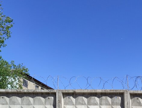 Barbed wire on concrete fence on a background of blue sky. Protecting the industrial enterprise, protection against intruders and danger, no trespassing. Illegal entry concept, immigration. Violation.