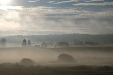 Beautiful autumn moody landscape - fields and houses of village shrouded in mist in the morning.