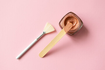 Facial pink clay mask for sensitive skin, wooden stick and make-up brush on pink background with...