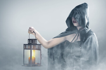 Asian witch woman with a cloak holding a lantern standing