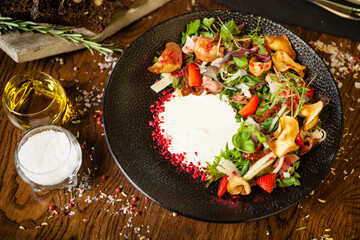 Crudo ham salad. Stracciatella and Grana Padano cheese, sundried tomato, fresh cucumber. Delicious healthy mixed greens food closeup served on a table for lunch in modern cuisine gourmet restaurant.