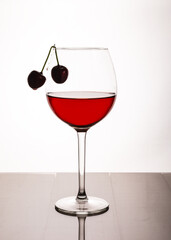 A thin-stemmed glass with red wine and a cherry on the edge.