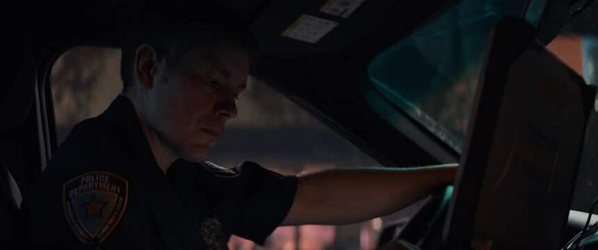Portrait of police officer talking on CB radio while checking records on a laptop inside a car