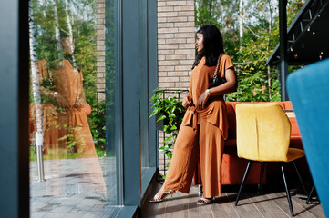 Portrait of beauty young black woman, wear orange outfit, pose at restaurant.