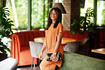 Portrait of beauty young black woman, wear orange outfit, pose at restaurant.