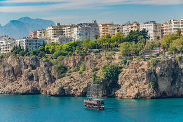 View of waterfall at Mediterranean seacoast cliff and beach near Antalya and big tour boat...