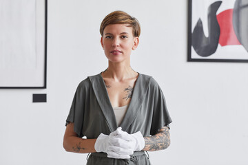 Waist up portrait of tattooed creative woman looking at camera while standing against white wall in...