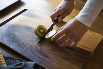 キウイフルーツを包丁で切り、調理する女性の手元