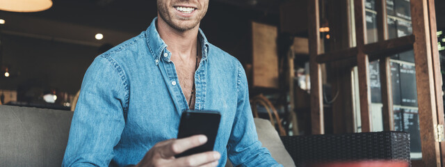 Smiling entrepreneur working on business project in city cafe, using mobile phone. Wide screen,...
