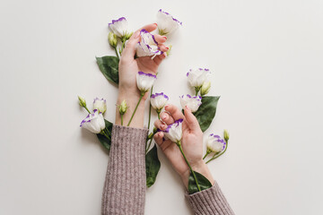 Delicate hands and spring flowers of eustoma are on the white table. the concept of skin care. Natural cosmetics for hand skin care. Natural flower extract cosmetics, beauty and fashion